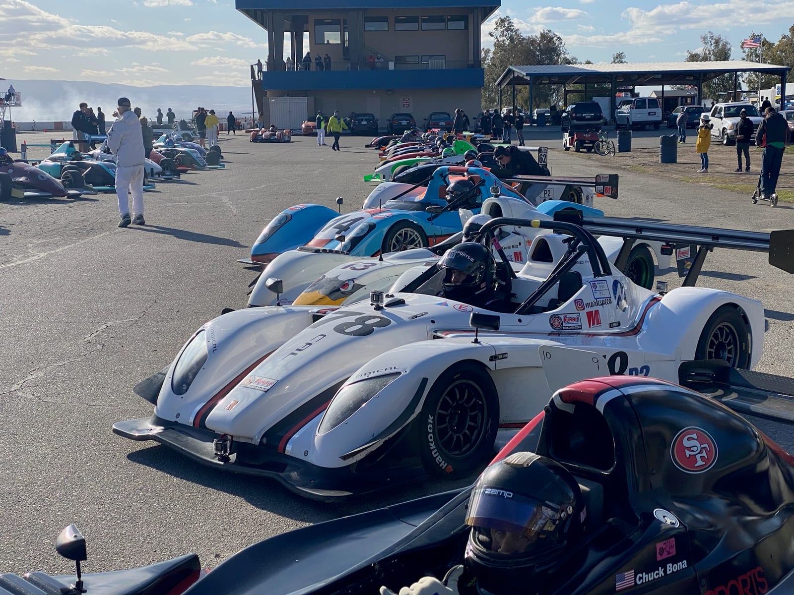 A row of Radical sports racers staged in the paddock on race day with crew and tower behind.